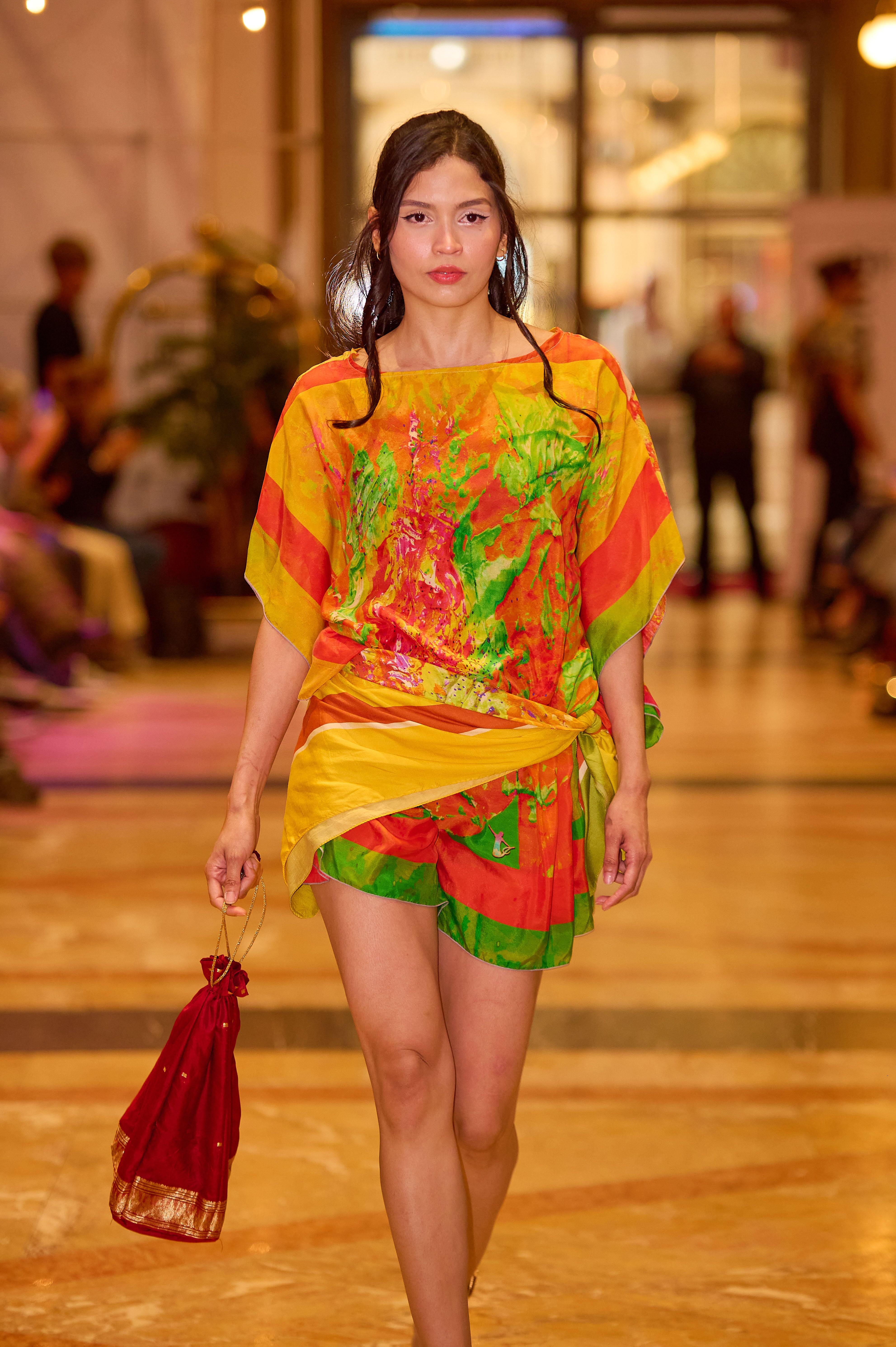 Model wearing a silk painted wrap with an upcycled bag on a runway.